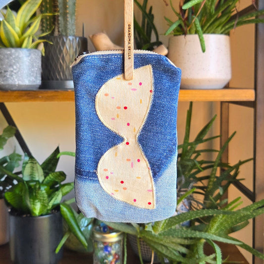 Hand holding a small blue pouch with a white design against a plant-filled background