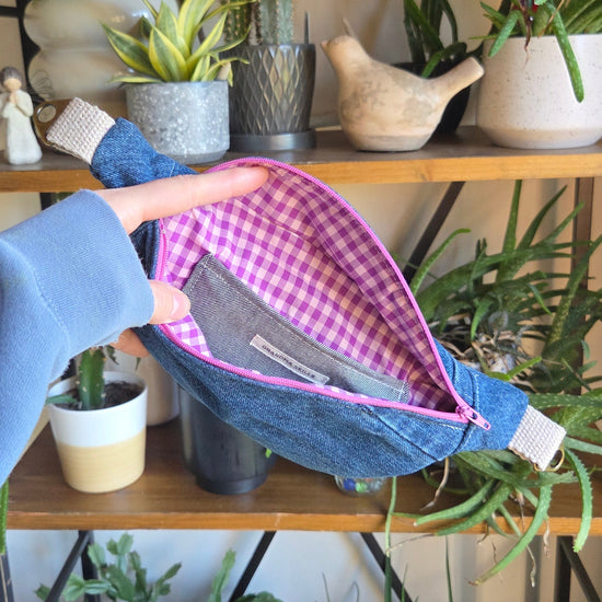 Person holding an upcycled denim fanny pack with a checkered interior against a plant-themed background